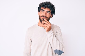 Handsome young man with curly hair and bear wearing casual winter sweater thinking concentrated about doubt with finger on chin and looking up wondering