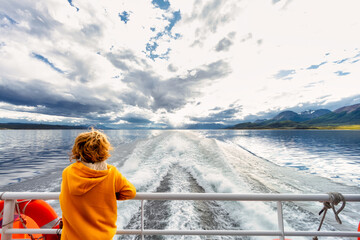 Child contemplates the landscape of the Beagle Channel from the stern of a ferry boat during a tour - obrazy, fototapety, plakaty