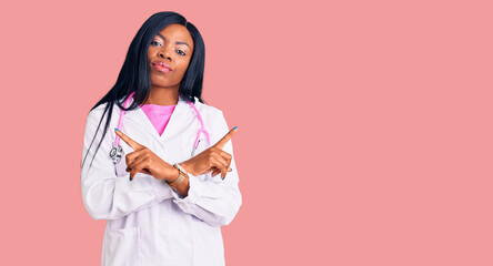 Fototapeta premium Young african american woman wearing doctor stethoscope pointing to both sides with fingers, different direction disagree
