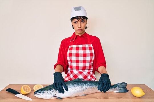 Beautiful brunettte woman fishmonger cooking fresh raw salmon skeptic and nervous, frowning upset because of problem. negative person.