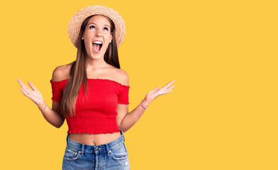 Young beautiful hispanic woman wearing summer hat crazy and mad shouting and yelling with aggressive expression and arms raised. frustration concept.