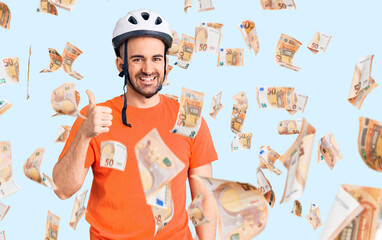 Young handsome man wearing bike helmet smiling happy and positive, thumb up doing excellent and approval sign