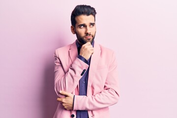 Young handsome man with beard wearing elegant jacket with hand on chin thinking about question, pensive expression. smiling with thoughtful face. doubt concept.