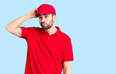 Young handsome man with beard wearing delivery uniform confuse and wondering about question. uncertain with doubt, thinking with hand on head. pensive concept.