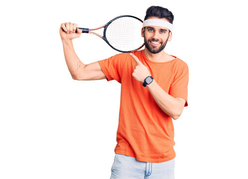 Young handsome man with beard playing tennis holding racket smiling happy pointing with hand and finger