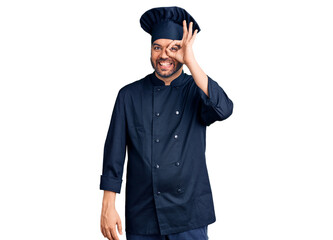 Young hispanic man wearing cooker uniform doing ok gesture with hand smiling, eye looking through fingers with happy face.