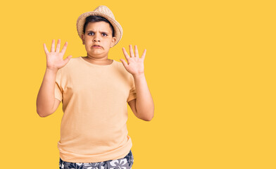 Little boy kid wearing summer hat and hawaiian swimsuit afraid and terrified with fear expression stop gesture with hands, shouting in shock. panic concept.