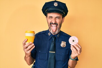 Middle age hispanic man wearing police uniform eating take away coffee and donut sticking tongue...