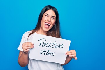 Young beautiful woman asking for optimist attitude holding paper with positive vibes message looking positive and happy standing and smiling with a confident smile showing teeth