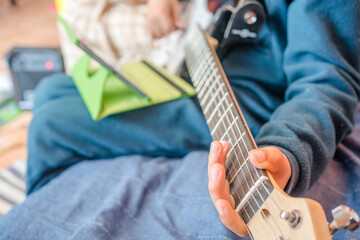 Closeup on child playing, holding, learning an electric guitar music class background.