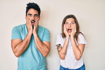 Beautiful young couple of boyfriend and girlfriend together afraid and shocked, surprise and amazed expression with hands on face