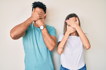 Beautiful young couple of boyfriend and girlfriend together covering eyes and mouth with hands, surprised and shocked. hiding emotion