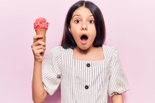 Beautiful child girl holding ice cream scared and amazed with open mouth for surprise, disbelief face