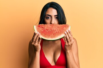 Beautiful hispanic woman putting watermelon slice as funny smile relaxed with serious expression on face. simple and natural looking at the camera. - obrazy, fototapety, plakaty