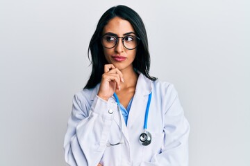 Beautiful hispanic woman wearing doctor uniform and stethoscope thinking concentrated about doubt...