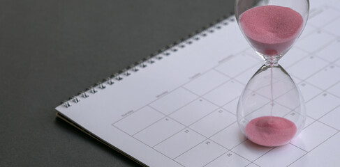 Hour glass with sand flowing,  sitting on calendar. Close up.