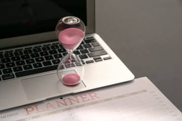 Hourglass on top of computer laptop and calendar planner