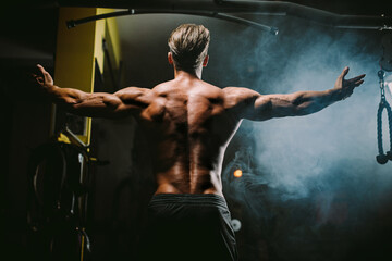 Fototapeta na wymiar muscular man posing in gym background. Fitness athlete man showing back muscles in gym. Muscular male shirtless posing with hands up. Black background.