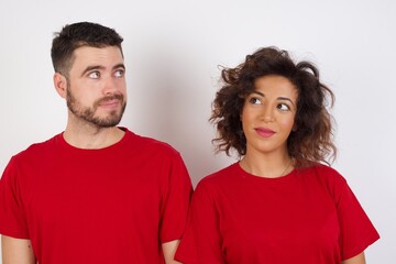 Fototapeta premium Young beautiful couple wearing red t-shirt on white background, looking aside into empty space thoughtful