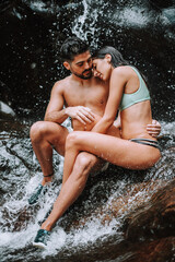 Obraz premium Pareja en un lago bajo una cascada en plena naturaleza disfrutando de una ruta en su viaje de vacaciones