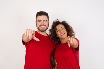 Naklejka premium Young beautiful couple wearing red t-shirt on white background pointing at camera with a satisfied, confident, friendly smile, choosing you
