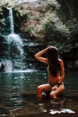 Chica joven atractiva en lago posando sobre una piedra