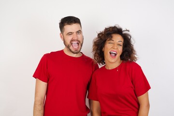 Young beautiful couple wearing red t-shirt on white background winking looking at the camera with sexy expression, cheerful and happy face.