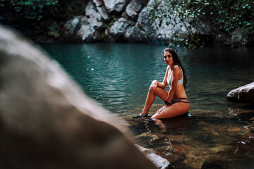 Fototapeta premium Chica atractiva morena sobre roca en lago