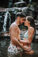 Pareja en un lago bajo una cascada en plena naturaleza disfrutando de una ruta en su viaje de vacaciones