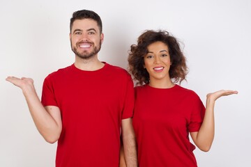 Cheerful cheery optimistic Young beautiful couple wearing red t-shirt on white backgroundholding two palms copy space