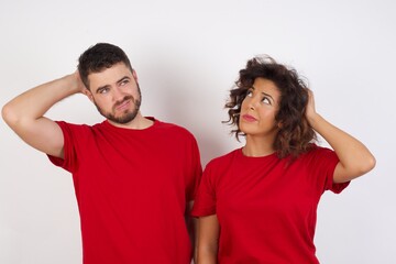 Young beautiful couple wearing red t-shirt on white background confuse and wonder about question. Uncertain with doubt, thinking with hand on head. Pensive concept.