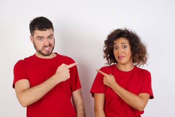 Fototapeta premium Young beautiful couple wearing red t-shirt on white background Pointing aside worried and nervous with forefinger, concern and surprise concept.