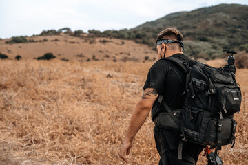 Joven explorador fotografo camina por medio de un valle seco en la naturaleza con su equipo fotografico
