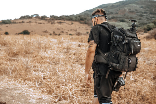 Joven explorador fotografo camina por medio de un valle seco en la naturaleza con su equipo fotografico