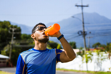 portrait of latino bespectacled man drinking a drink to hydrate himself while exercising.
