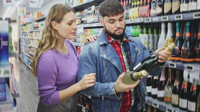 Portrait of young man and woman choosing bottle of cava in grocery shop