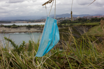 image of a protective mask hanging from a branch with a sea background with clouds and blue sky