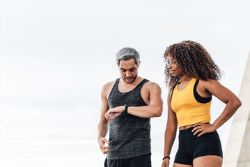 Two fit athlete couple of friends taking a rest after hard running session looking at their wearable tech sports watch - Focus on man face