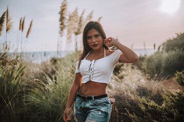 Chica veraniega morena en la playa naturaleza cañas de bambu con skateboard y bikini disfrutando de la hora dorada del atardecer