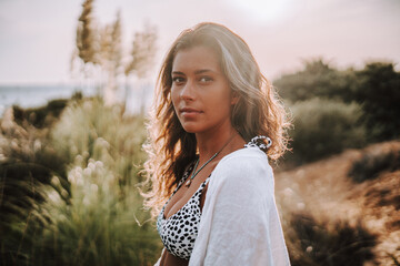 Chica veraniega morena en la playa naturaleza cañas de bambu con skateboard y bikini disfrutando de la hora dorada del atardecer
