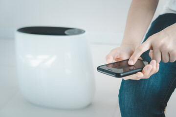 Fototapeta premium Woman control a modern air purifier through the application on a smartphone, a smartphone screen isolated in white color. Modern and smart home connectivity technology concept.