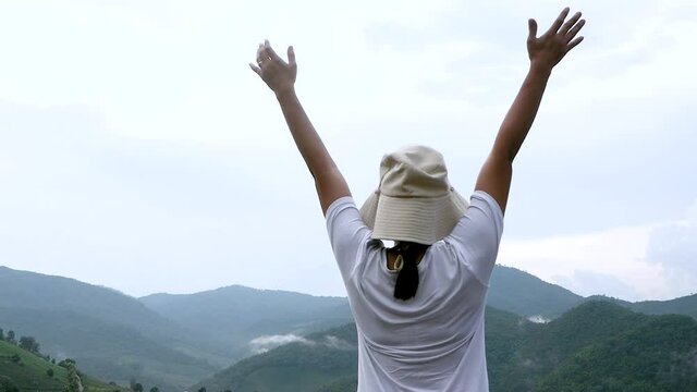 Back view of cheerful young woman  with her arms outspread on peak of mountain with sky background. Achievement and winning concept.