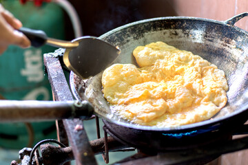 .Omelet fried in oil is boiling in an old pan on a gas stove.