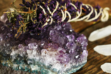 A close up image of an amethyst geode and lilac smudge stick with clear quartz crystals on a dark...