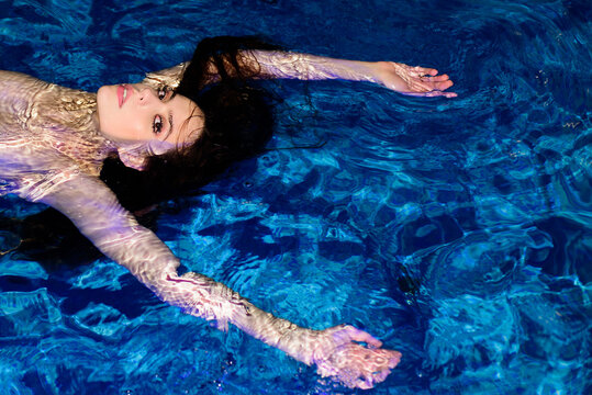 Young attractive woman in in pool. Fashion photo of sexy beautiful girl model with dark hair swim on back in swimming pool with red lips and sensual look.