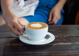 closeup of hand holding late forming hot coffee heart shape cup on wooden table with copy-space