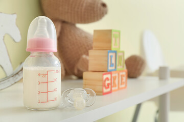 Bottle of milk for baby, pacifier and toys on table