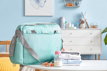Bottle of milk for baby with clothes and bag on table in room
