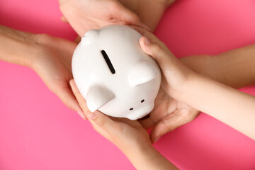 Hands of family with piggy bank on color background