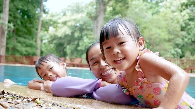 Happy young mother and her daughter smiling in swimming pool in a hot summer day. Family lifestyle in vacation.